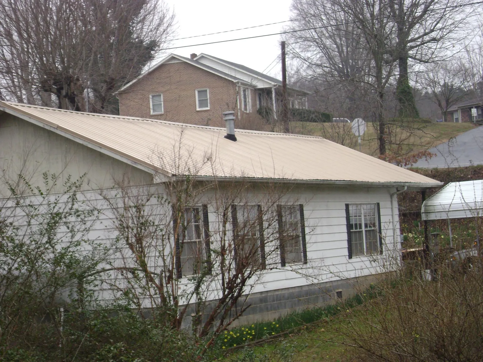 Tan metal roof on a white sided house set into a hillside — Commercial Roofing by Roofing Brothers in Springboro